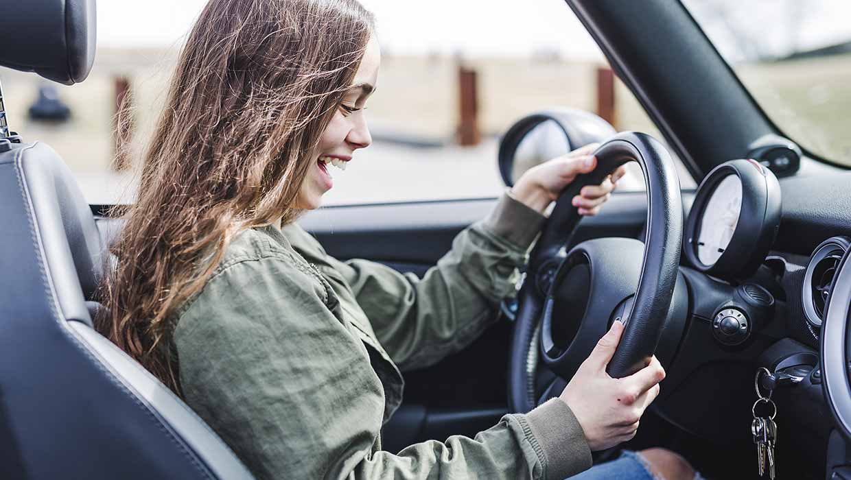 Junge glückliche Frau aum Steuer ihres ersten eigenen Autos.